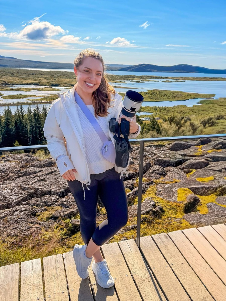 Katelynn holding a camera in front of a lake and mountains